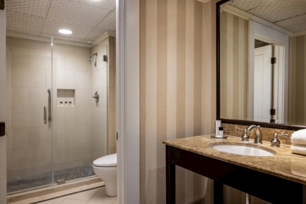 The image shows a modern bathroom with a glass-enclosed shower, a vanity with a marble countertop, a sink, a mirror, and neatly folded towels.