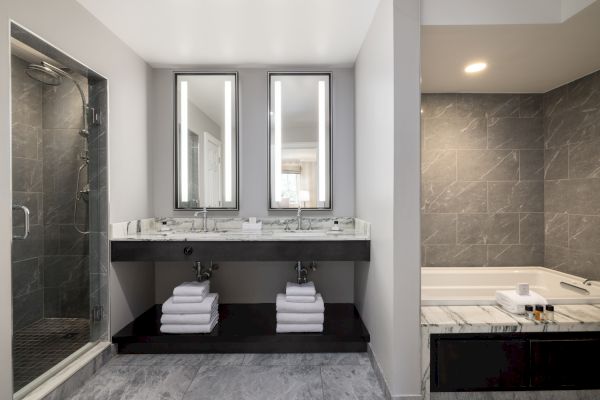 A modern bathroom with a glass-enclosed shower, double sink vanity with mirrors, and a bathtub. Towels and toiletries are neatly arranged.