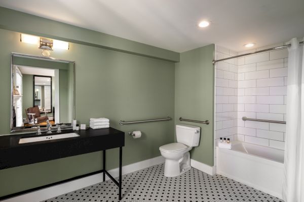 A bathroom with green walls, a sink with a mirror, a toilet, and a bathtub with a shower curtain. There are grab bars by the toilet and bathtub.