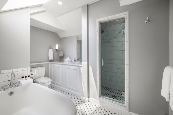 This image shows a modern bathroom with a bathtub, toilet, sink with mirror, and a tiled shower enclosure. The walls and floor are decorated in white and gray.