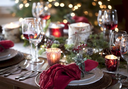 A festive dinner table setup with red napkins, wine glasses, candles, and holiday decorations, including greenery and lights.