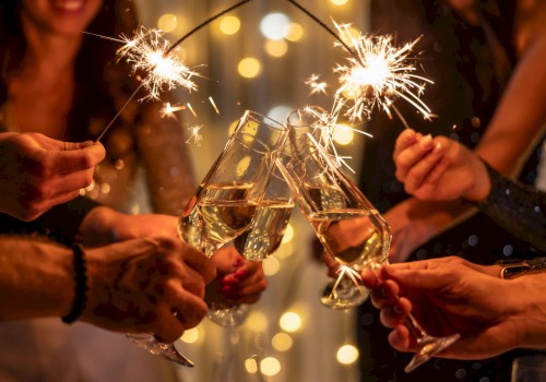 Group of people toasting with sparklers and champagne flutes, celebrating under warm fairy lights.