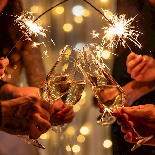 Group of people toasting with sparklers and champagne flutes, celebrating under warm fairy lights.