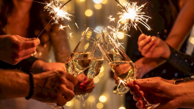 Group of people toasting with sparklers and champagne flutes, celebrating under warm fairy lights.