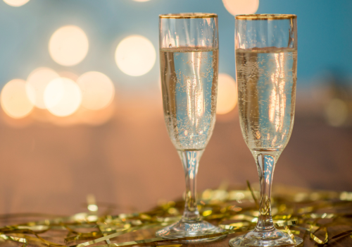 Two glasses of champagne with gold rims are set on a table decorated with gold streamers, with a blurred background of warm lights.