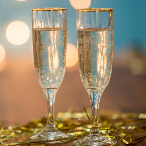 Two glasses of champagne with gold rims are set on a table decorated with gold streamers, with a blurred background of warm lights.