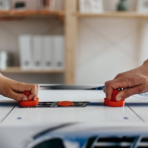 Two people are playing air hockey, each holding a paddle and aiming to hit the puck on the table.