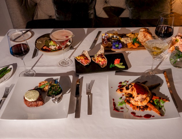 A table set with gourmet dishes, including stuffed peppers, a fancy chicken plate, and drinks, elegantly arranged for a dining experience.