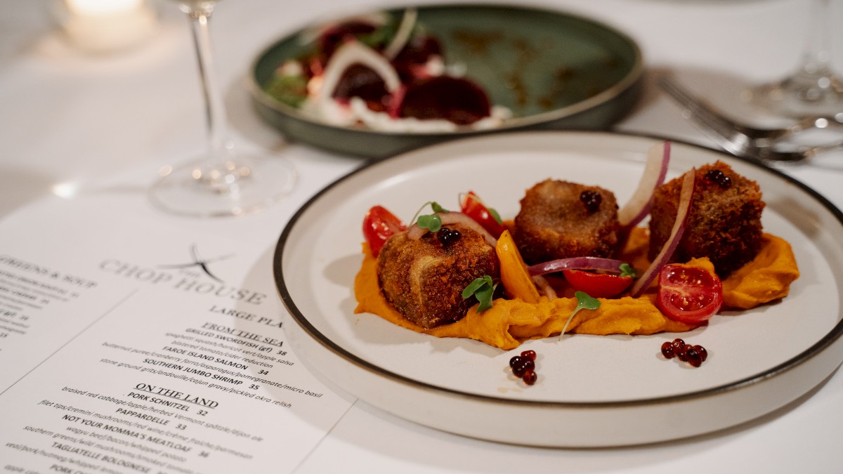 A beautifully plated dish of breaded meat with vegetables, served with a side salad and a drink at a fine dining restaurant.