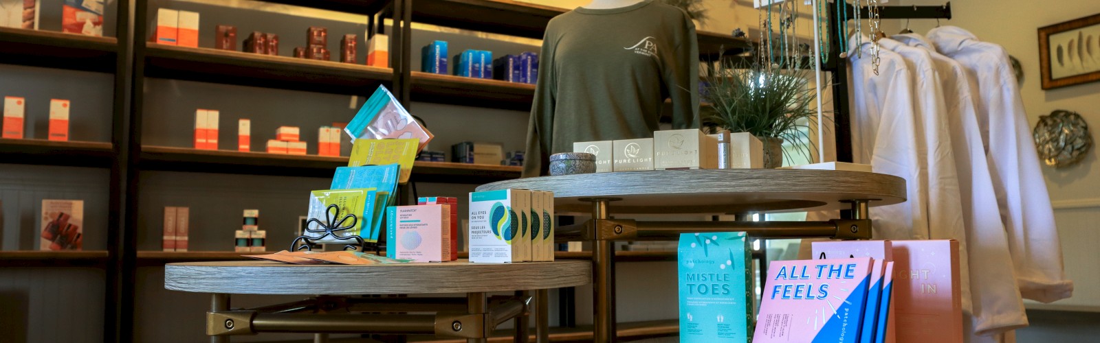 A boutique display with skincare products, clothing, and accessories set on tables and shelves with decorative plants in the background.