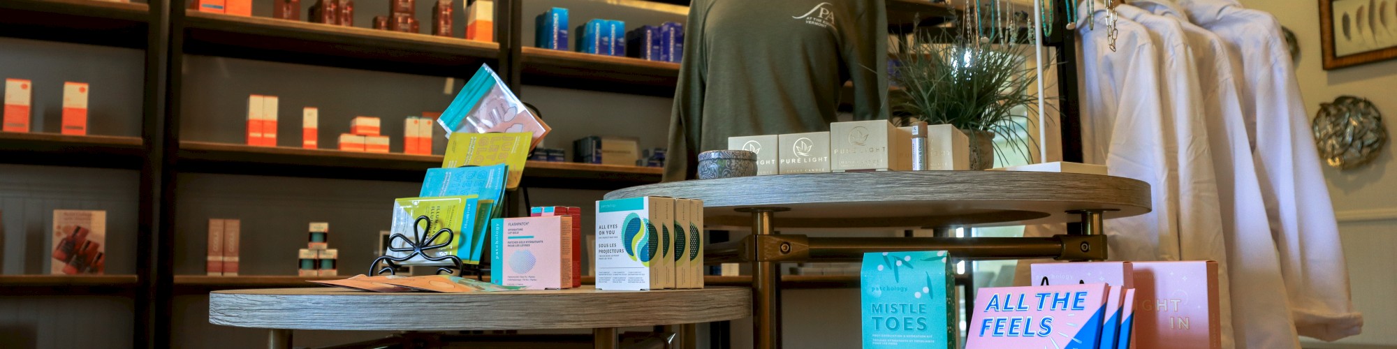 A boutique display with skincare products, clothing, and accessories set on tables and shelves with decorative plants in the background.