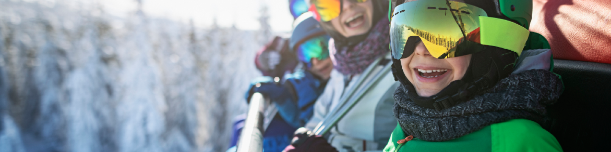 A group of skiers in colorful gear enjoying a sunny day on a ski lift, with snow-covered trees in the background.