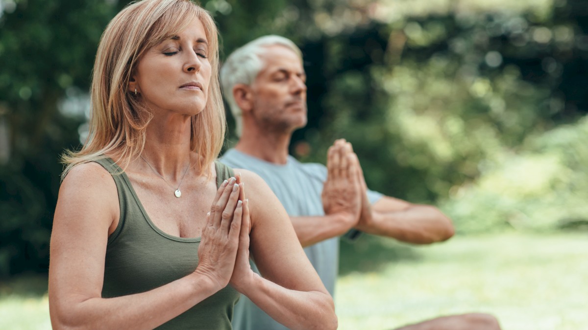 Two people are meditating outdoors with their hands in a prayer position.