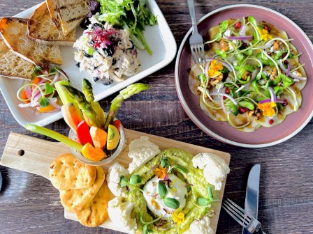 The image shows a table with assorted dishes including salads, fresh vegetables, dips, and bread. It appears to be a colorful, healthy meal setup.