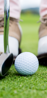 Golf ball near hole, club, golfer's shoes; putt on the green.