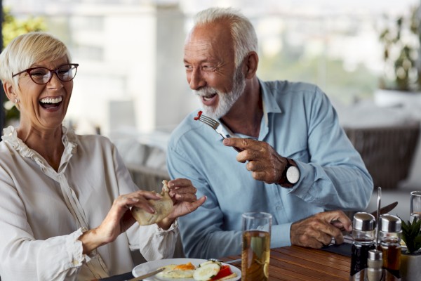 Two elderly individuals are joyfully interacting at a table while enjoying a meal together. They both appear to be laughing and having a good time.