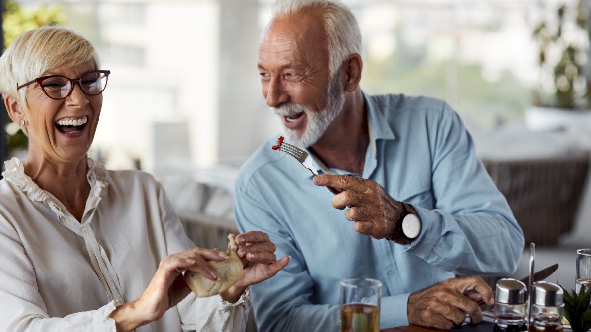 Two happy elderly people are sharing a light-hearted moment while dining.