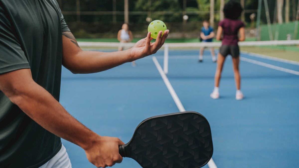 People playing pickleball on a blue court with paddles and a yellow ball, preparing for a serve.