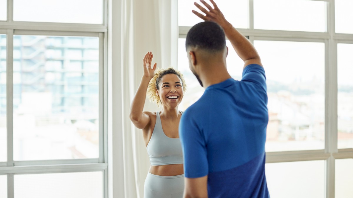 Two people in athletic wear are giving each other a high-five in a bright room with large windows.