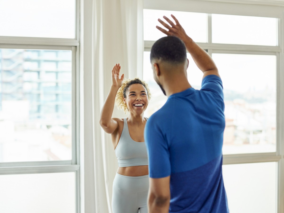 Two people in athletic wear are giving each other a high-five in a bright room with large windows.