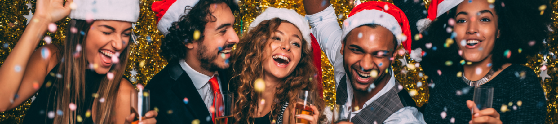 A group of five people wearing Santa hats are celebrating, holding drinks and smiling with a gold sequin background and festive atmosphere.