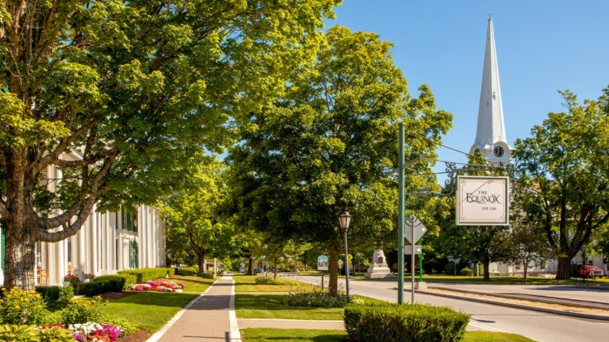 A scenic street view with lush green trees, a sidewalk, neatly landscaped areas, and a white church steeple in the background, ending the sentence.