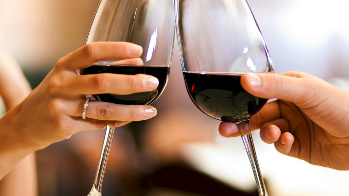 Two hands clinking glasses of red wine in a celebratory toast, creating a festive atmosphere.