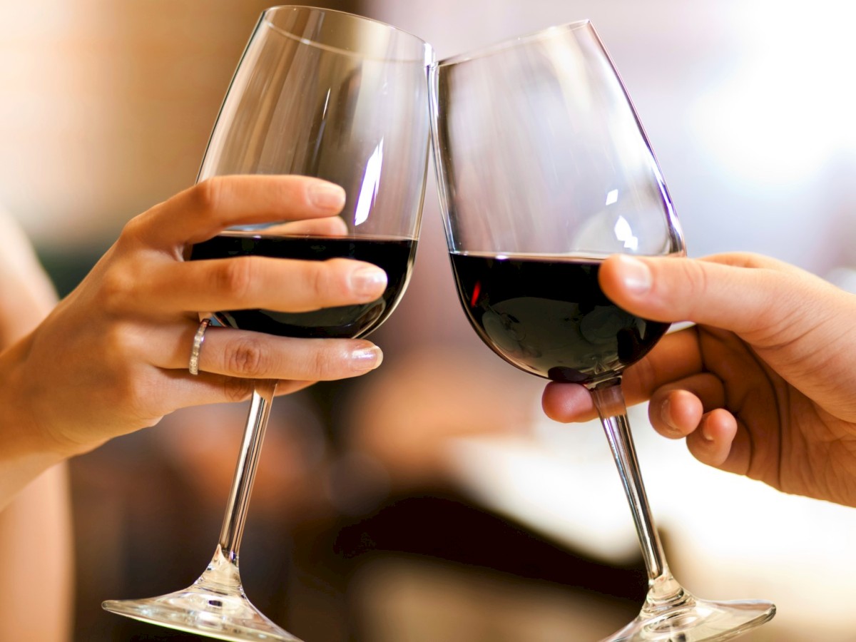 Two hands clinking glasses of red wine in a celebratory toast, creating a festive atmosphere.