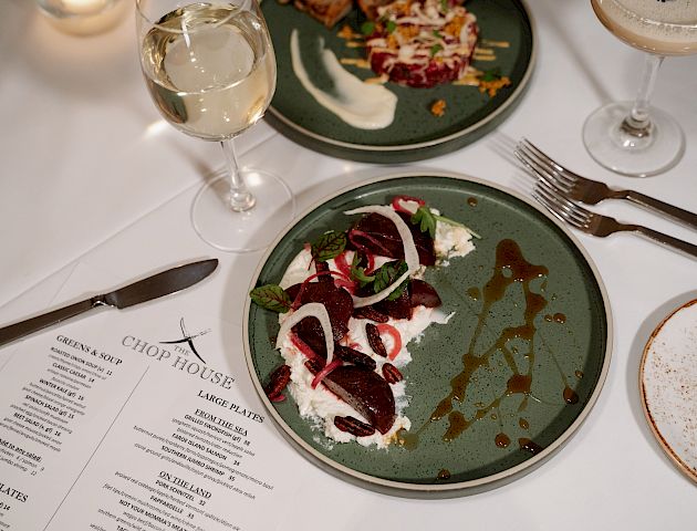 A restaurant table setting with plates of food, a menu, wine glasses, and cutlery on a white tablecloth, ended the sentence.