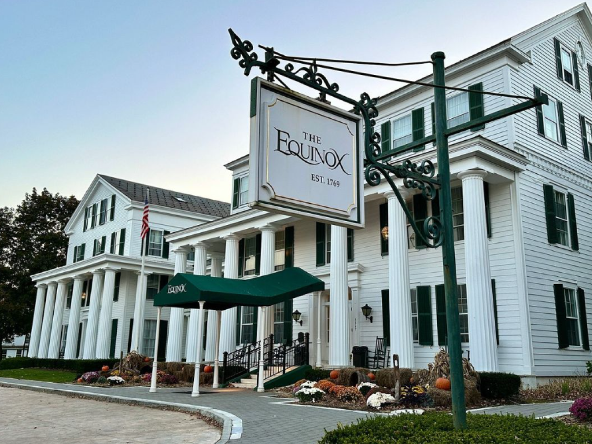 The image features a large white colonial-style building with a sign reading 