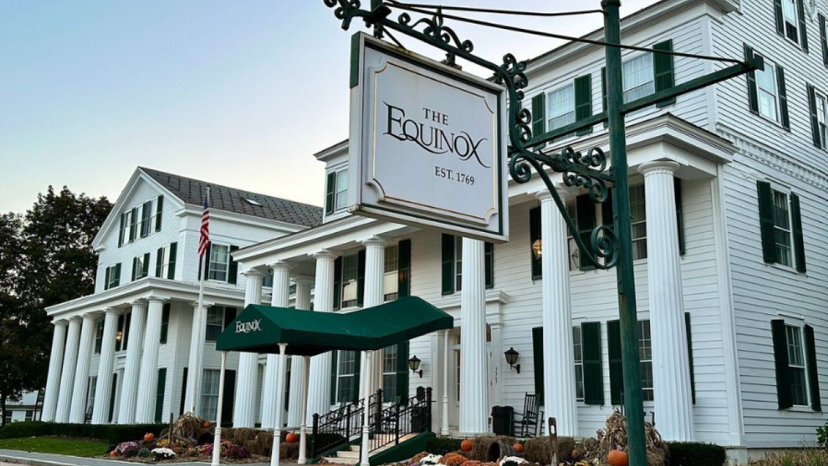 A large white building with columns, green shutters, and an awning. A sign reads 