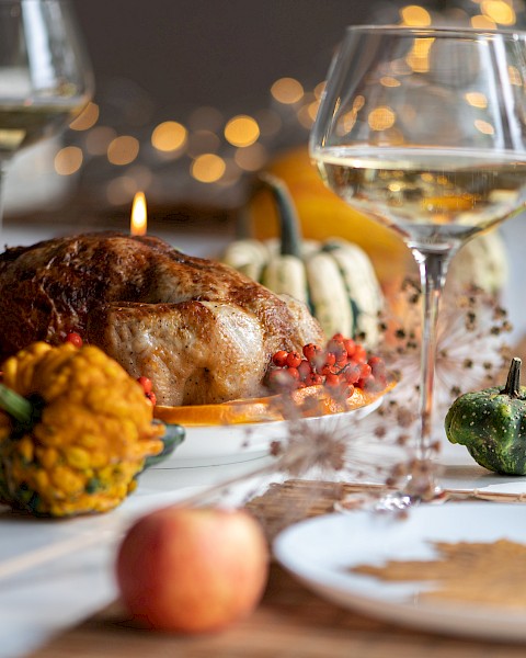 A Thanksgiving dinner table setup with roasted turkey, squash, wine glasses, and festive decorations, creating a cozy, autumn-themed ambiance.