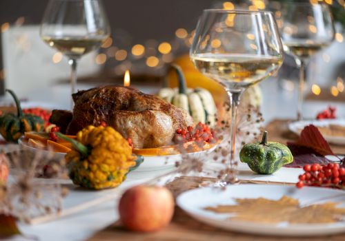 A Thanksgiving dinner table setup with roasted turkey, squash, wine glasses, and festive decorations, creating a cozy, autumn-themed ambiance.