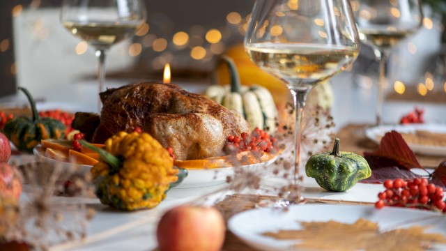 A Thanksgiving dinner table setup with roasted turkey, squash, wine glasses, and festive decorations, creating a cozy, autumn-themed ambiance.