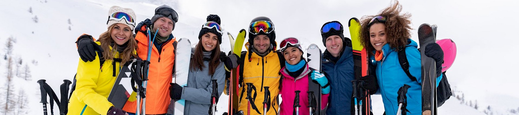 A group of people in colorful ski outfits posing with their skis on a snowy mountain.