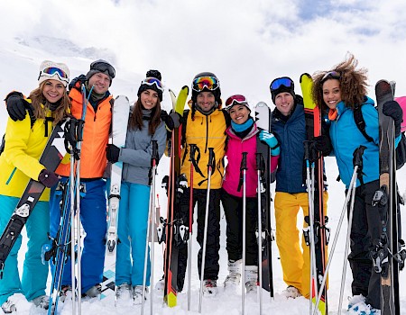 A group of people in colorful ski outfits posing with their skis on a snowy mountain.