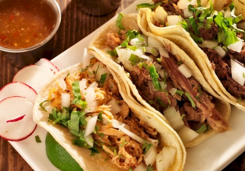 Three tacos with various meats, topped with cilantro and onions, served with sliced radishes and two small bowls of salsa.