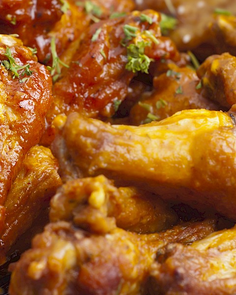 The image shows a plate of saucy chicken wings garnished with herbs.