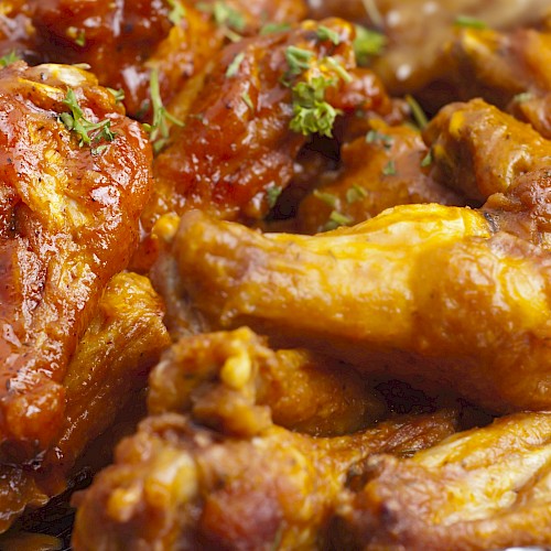 The image shows a plate of saucy chicken wings garnished with herbs.