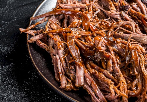 The image shows a plate of pulled pork with a rich, brown sauce, placed on a dark surface.