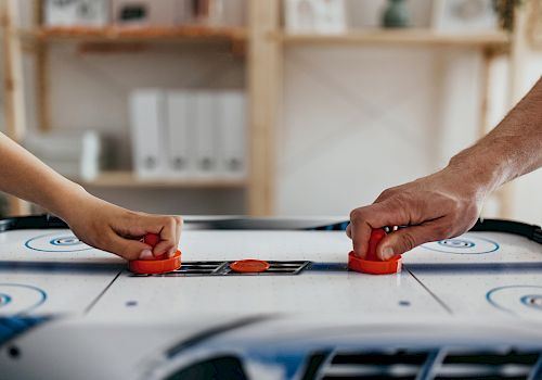 Two people are playing air hockey, each holding a paddle and aiming to hit the puck on the table.