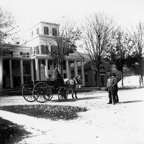 The image shows a historical scene with two men and a horse-drawn carriage in front of a large building with columns.