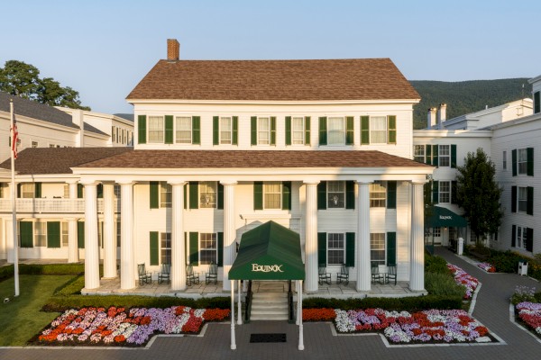 A grand white building with green shutters, classical columns, and vibrant flower gardens, possibly a hotel or historic estate.