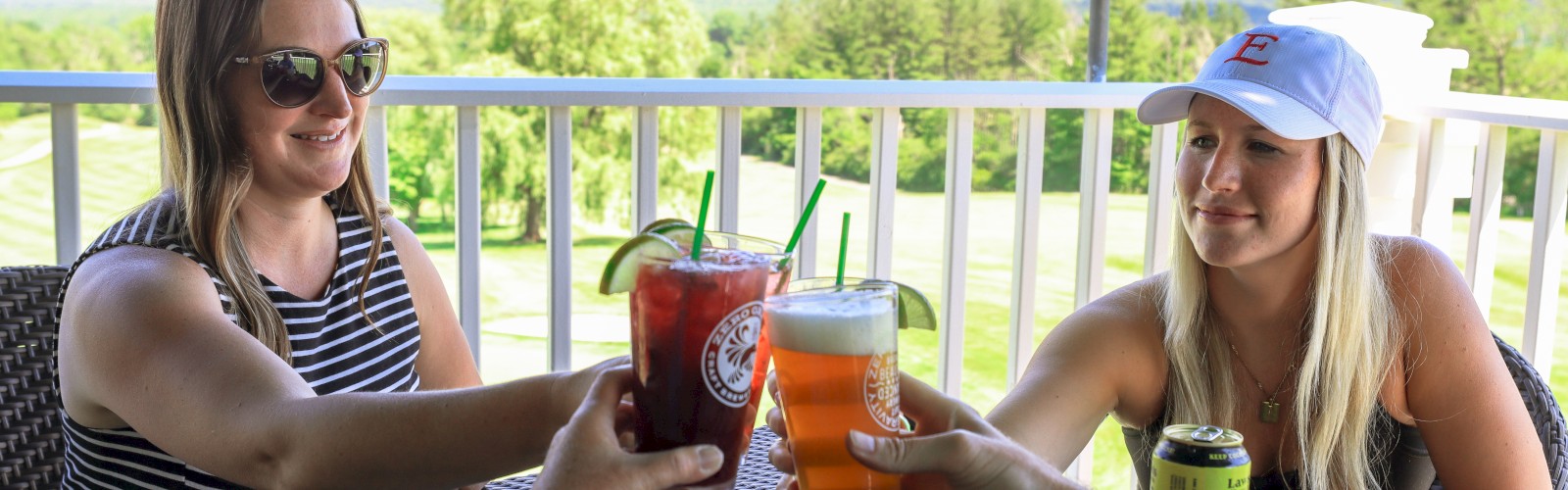People are toasting with drinks on a patio, enjoying a scenic view of mountains and greenery.