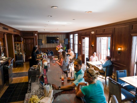 inside of room with people sitting at a bar and a musician playing the gutiar on back corner