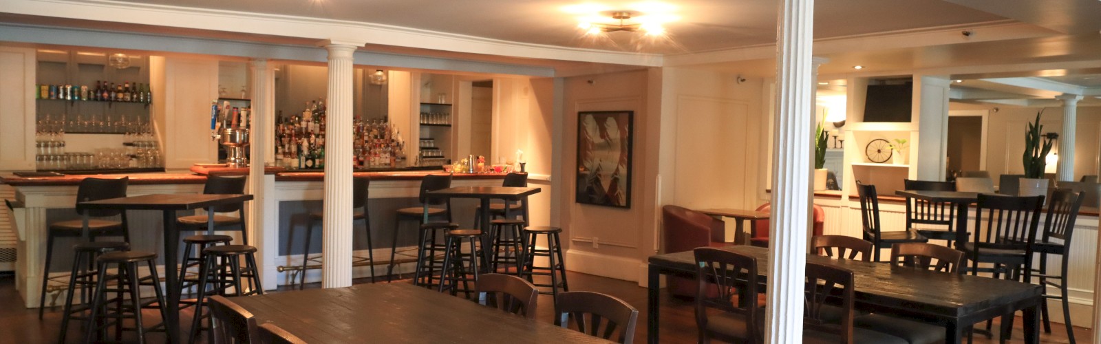 The image shows a spacious restaurant interior with wooden tables, chairs, and a bar area, creating a cozy dining atmosphere.