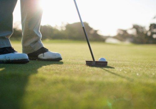 A person is putting a golf ball on a golf course, with the sun low in the sky.