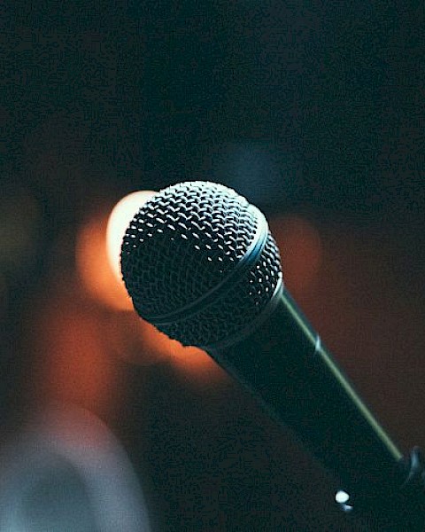 A microphone is shown against a dimly lit background, suggesting a performance or speech setting, captured with a warm tone.