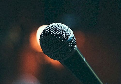 A microphone is shown against a dimly lit background, suggesting a performance or speech setting, captured with a warm tone.