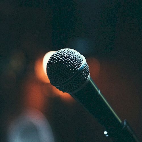 A microphone is shown against a dimly lit background, suggesting a performance or speech setting, captured with a warm tone.